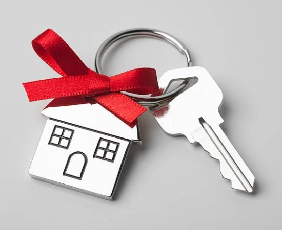 House keys with house shaped keychain with red ribbon on light grey background